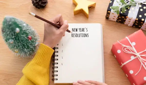 Mano escribiendo resoluciones de año nuevo en un cuaderno