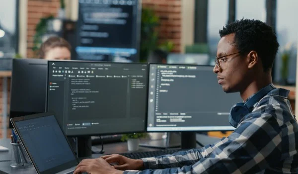 Un desarrollador que trabaja en una computadora portátil con dos unidades de visualización a la derecha