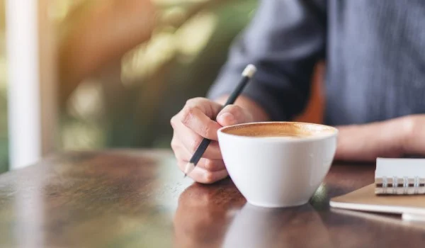 Una persona que sostiene un lápiz y una taza de café sobre la mesa.