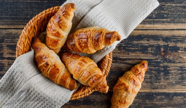 Cesta con cuatro croissants y otro croissant sobre la mesa