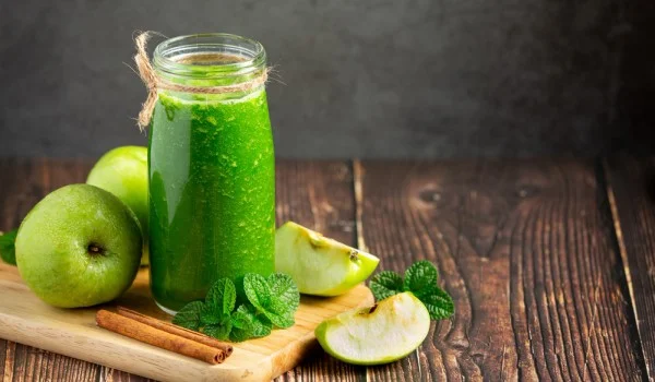 Un tarro de jugo verde con manzanas verdes y rodajas de manzana verde