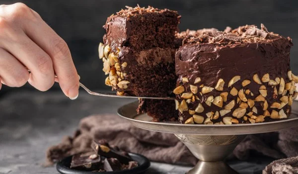 Una mano tomando un trozo de pastel de un pastel de chocolate entero