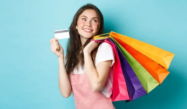 Una mujer que sostiene una tarjeta de regalo y varias bolsas de compras.