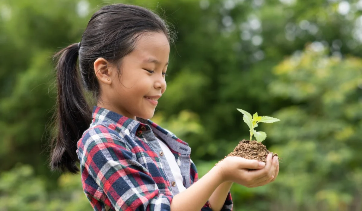 Chica sosteniendo una pequeña planta en su mano