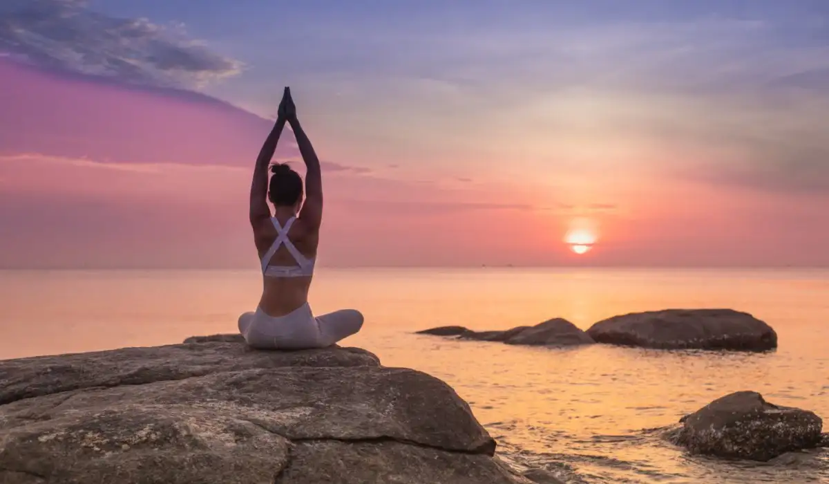 Una mujer meditando y haciendo yoga en frente del océano