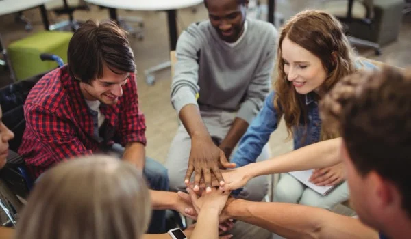 Un grupo de personas con las manos una encima de la otra señalando colaboración