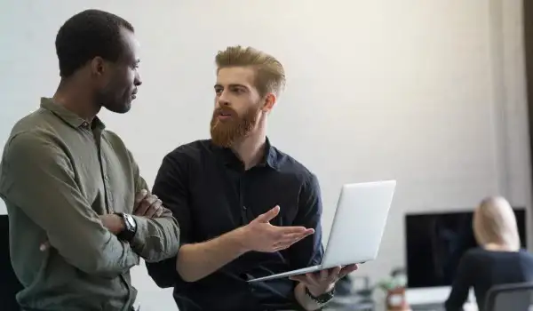 Dos personas conversando, mientras una sujeta una laptop